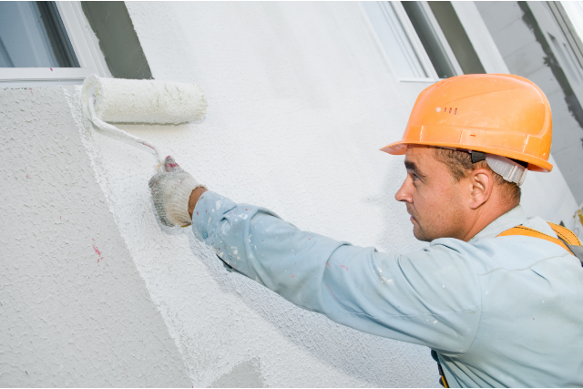 Exterior Painter with orange hard hat on and roller painting exterior wall